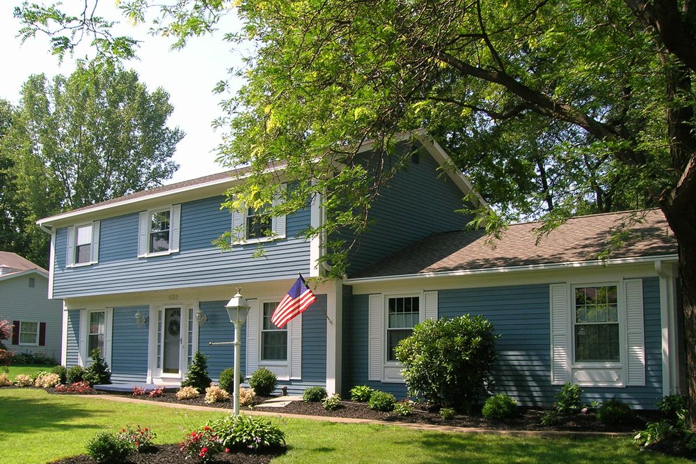 Blue colonial home refinished with white porch and flag