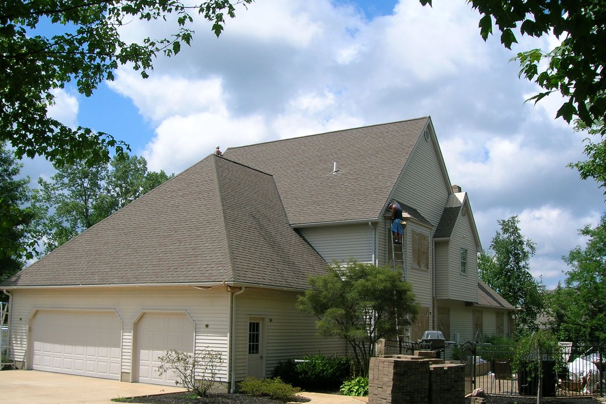 The same Erie home before — worn tan finish, crew masking and spraying